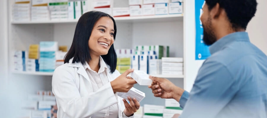 atendente de farmácia sorri e entrega um medicamento para o cliente 