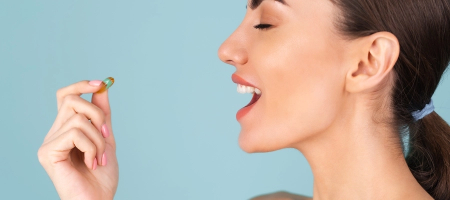 Mulher jovem com cabelos presos, olhos fechados e boca aberta, segurando um comprimido com os dedos, com dúvida se melatonina faz mal para o fígado.