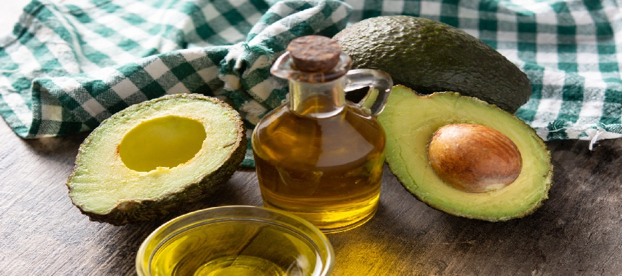 Metade de abacate fresco ao lado de garrafa de azeite sobre mesa rústica, representando fontes de gorduras boas.