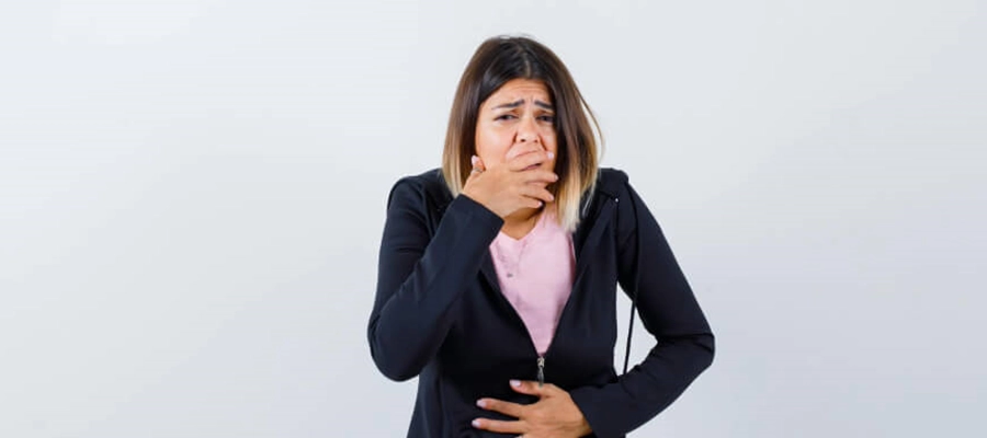 mulher com expressão de dor e nojo com uma mão tampando a boca e a outra sobre a barriga