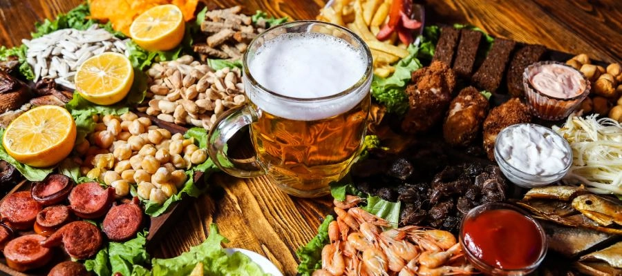 Copo de cerveja em meio a petiscos variados de comida de boteco, como salgadinhos e porções fritas, típicos de bares e encontros informais entre amigos.