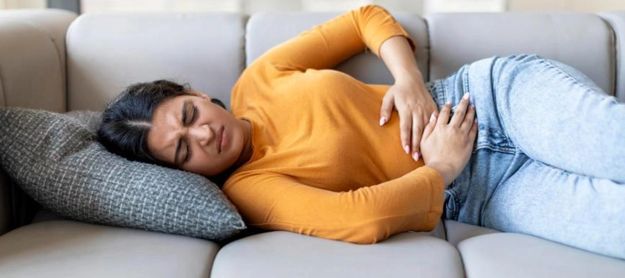 mulher deitada no sofá com expressão de desconforto e dor no estômago