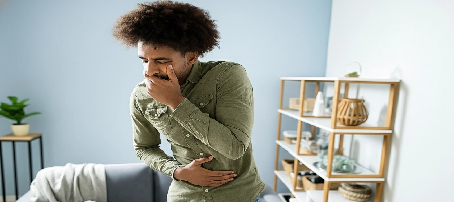 Homem jovem com expressão de mal-estar, segurando a barriga e a boca, em pé na sala de estar, indicando sintomas de intoxicação alimentar.