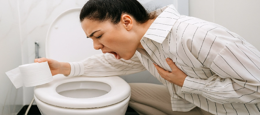 Mulher com expressão de mal-estar vomitando no vaso sanitário enquanto segura papel higiênico