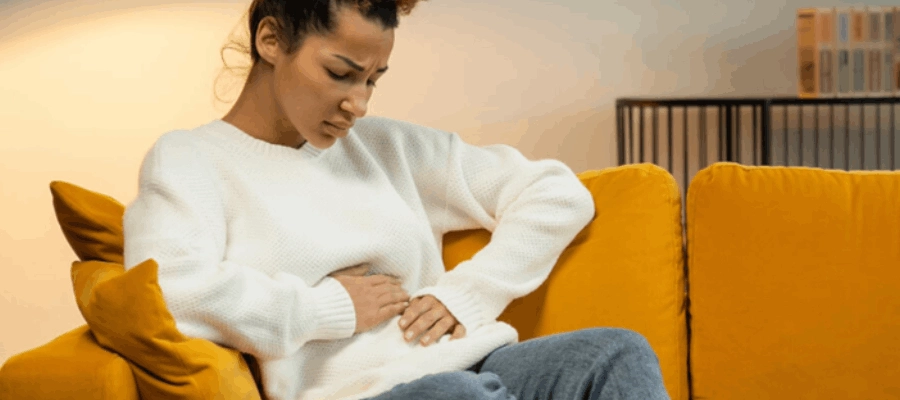 mulher com digestão lenta e expressão de desconforto abdominal sentada no sofá