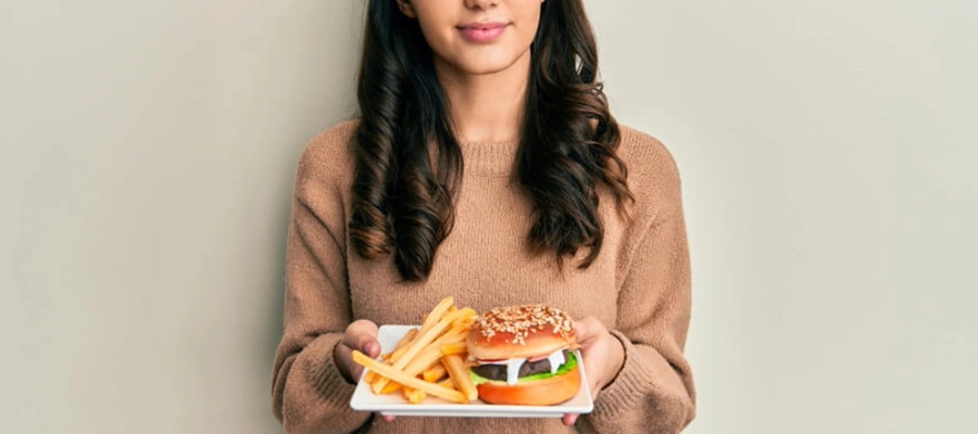 mulher jovem com cara prestativa segurando um prato com hambúrguer e batatas fritas.