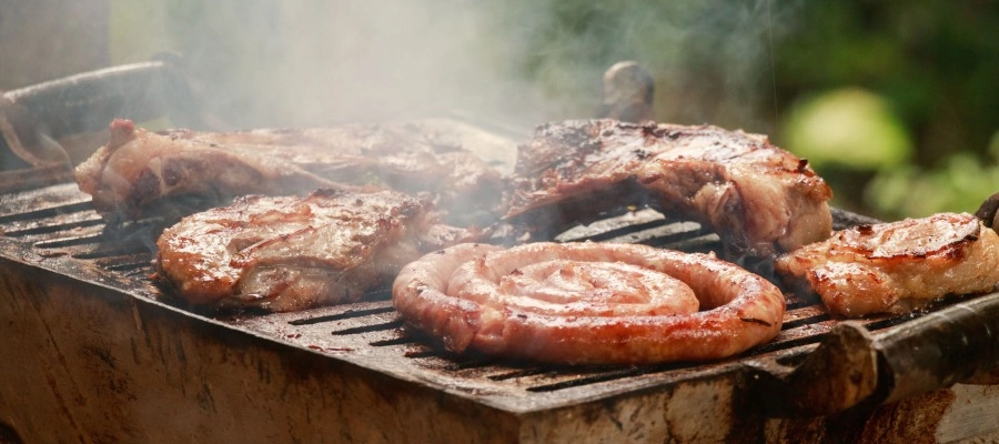 Churrasqueira com carnes gordurosas e linguiça em cima da grelha que podem causar enjoo após comer churrasco.
