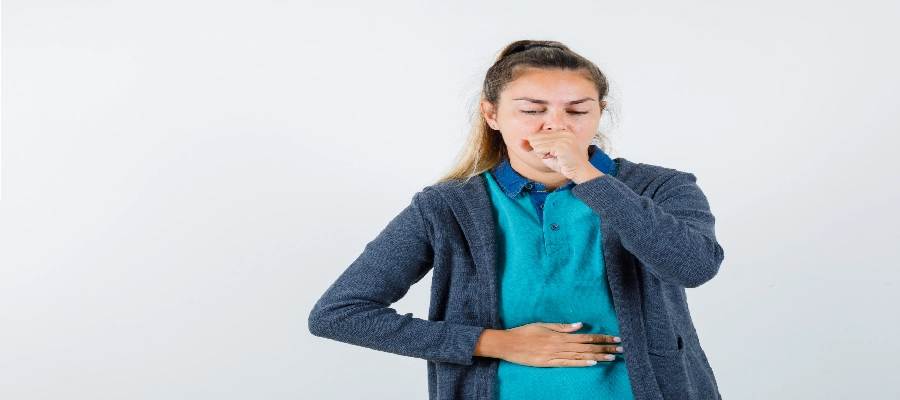 Mulher sentada no sofá com náusea, cobrindo a boca e segurando o abdômen com a outra mão, representando episódio de enjoo constante.