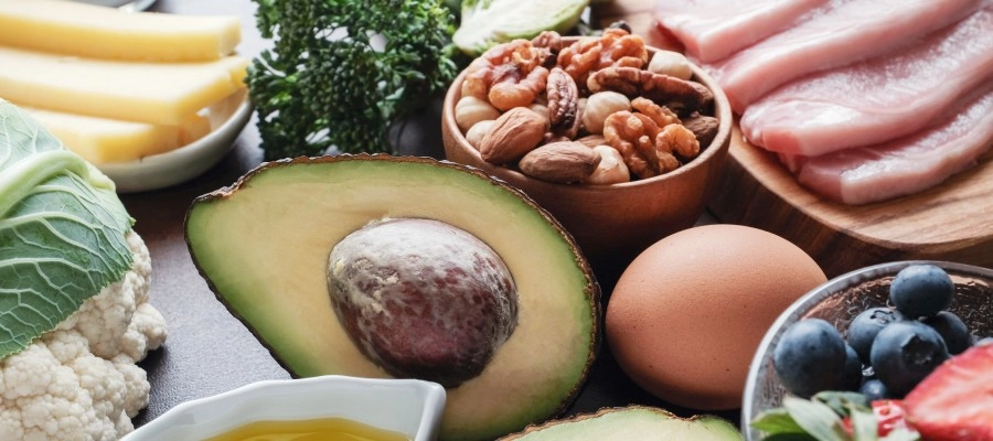 Mesa com alimentos da dieta cetogênica, como salmão, brócolis, mirtilos, ovos e azeite.