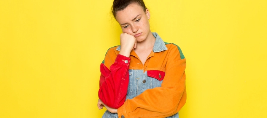 Mulher jovem com jaqueta colorida e camiseta amarela e expressão de mal-estar e reflexão sobre como melhorar o enjoo.