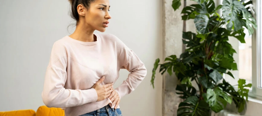 mulher olha pela janela e coloca as mãos na barriga por estar com dor